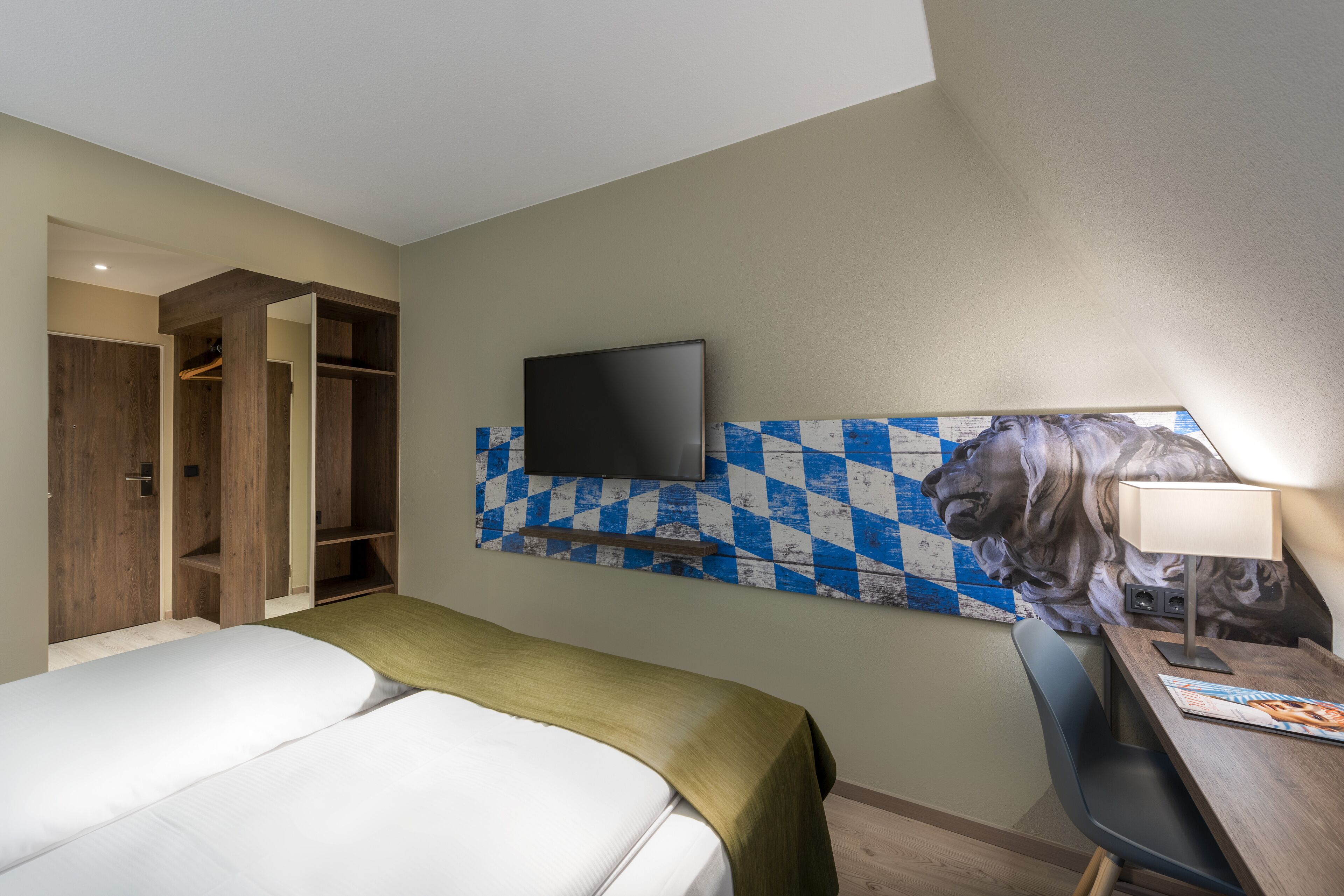 Una habitación de hotel con una cama, un escritorio con lámpara, televisión y armario.