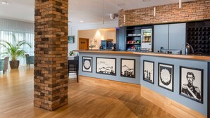 A reception area with a brick column, wooden reception desk, framed artwork, and a coffee machine. - ibis Styles Rosenheim (Rosenheim)