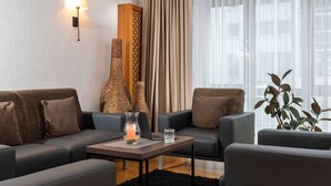 A modern living room with two sofas, a coffee table, a lamp, and a vase with flowers. - ibis Styles Rosenheim (Rosenheim)