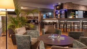A bar area with a brick wall, bar stools, and a TV mounted above the bar. - ibis Styles Rosenheim (Rosenheim)