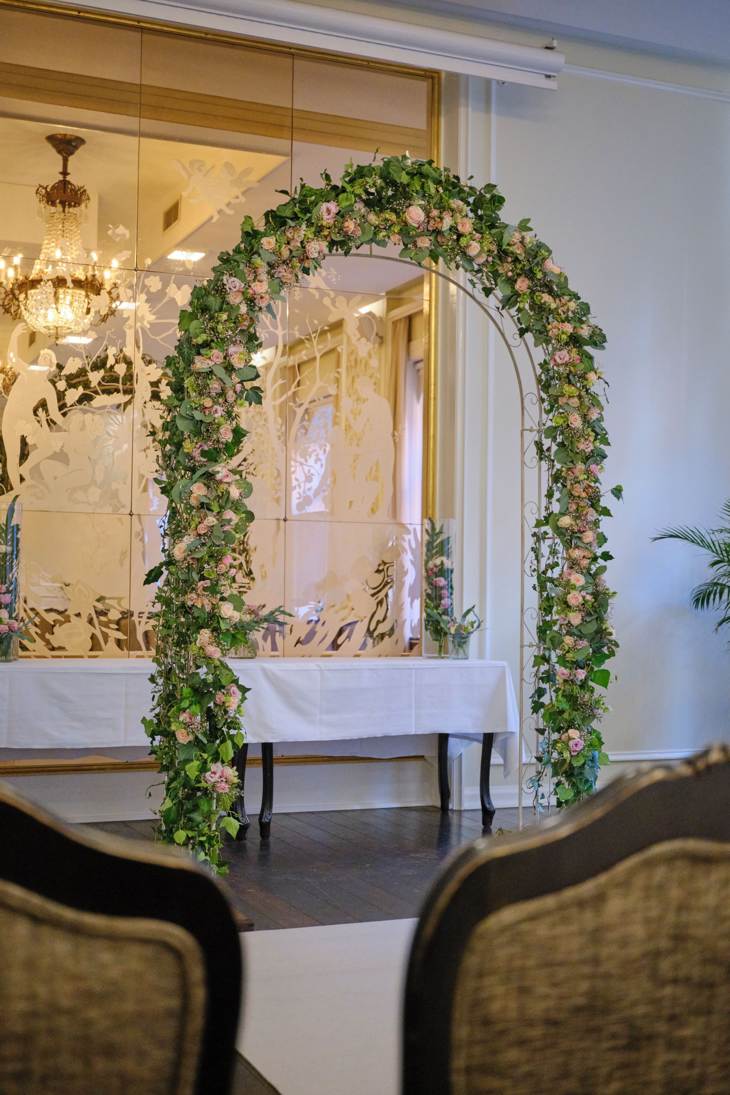 Una habitación con un arco floral, una mesa con mantel blanco y una araña.