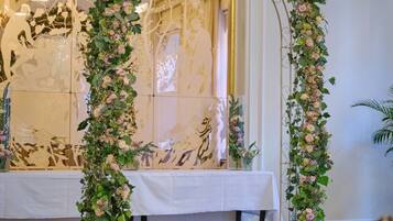 Una habitación con un arco floral, una mesa con mantel blanco y una araña.