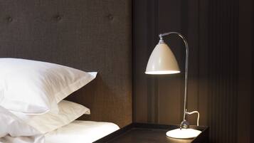 A neatly made bed with white linens and pillows, a dark headboard, and a bedside table with a white lamp.