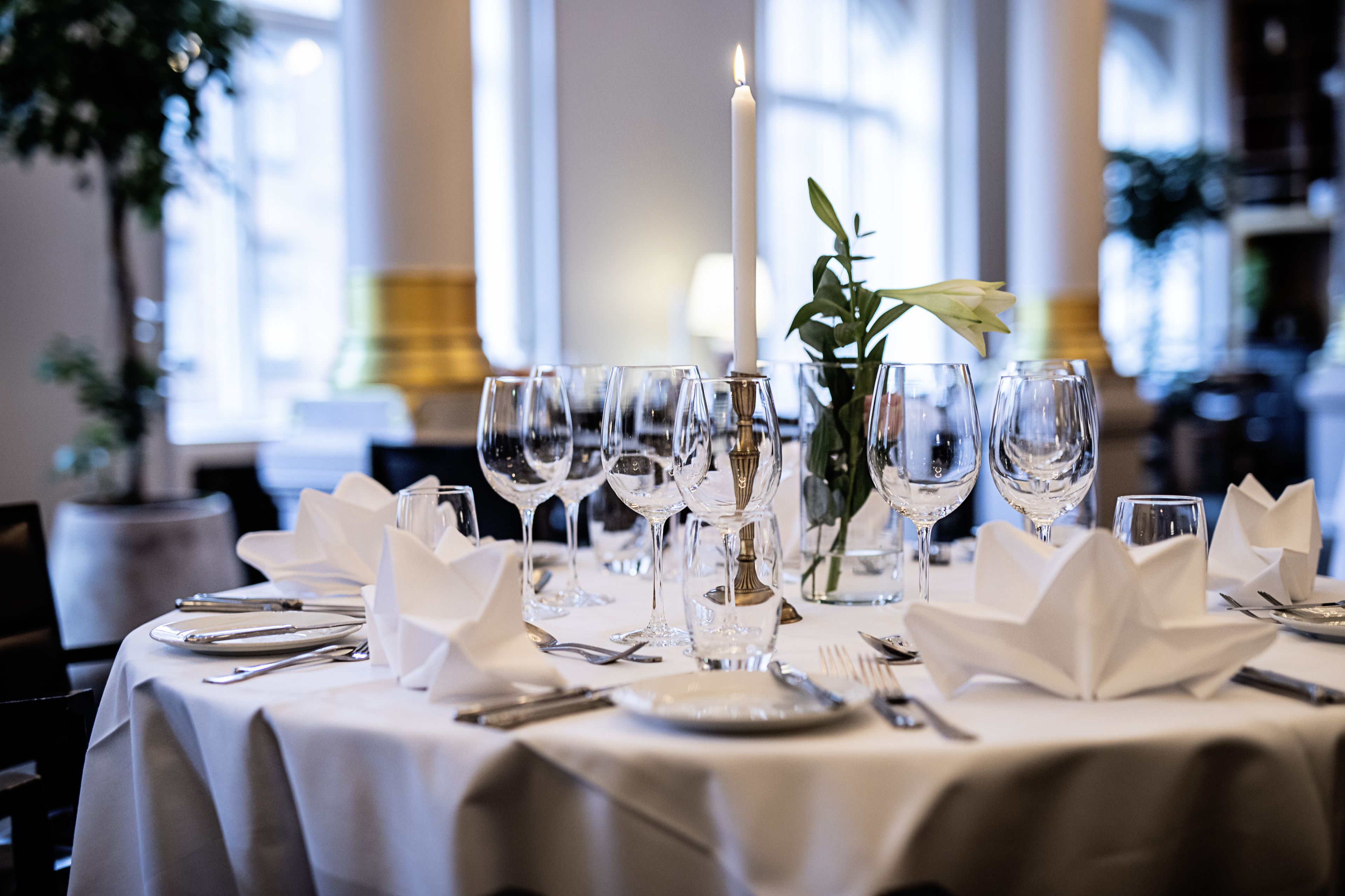 Taula posta per a sopar formal, amb diferents vasos de vi, plats i coberts, una espelma encèsa i un vas amb una planta.