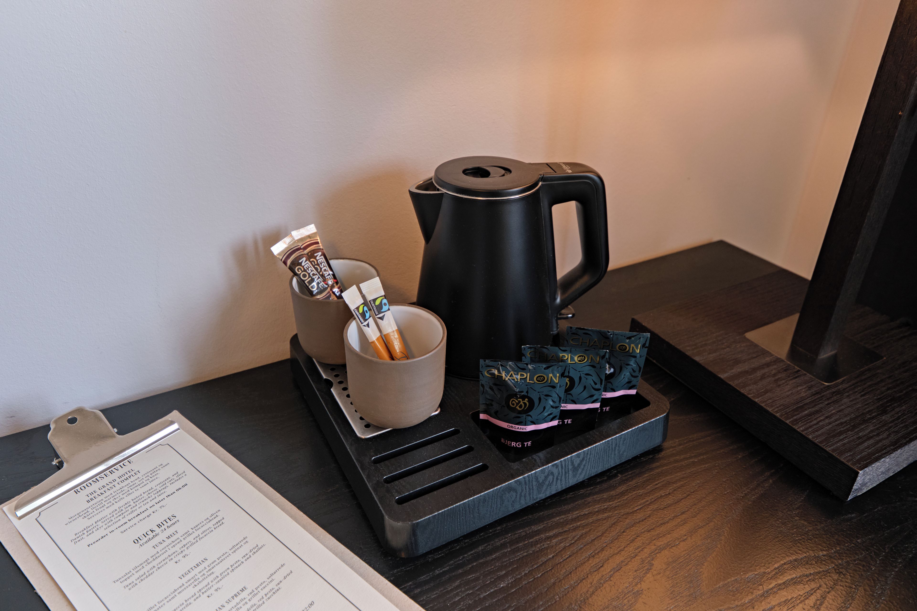 Eine Kaffeemaschine, eine Tasse und ein Tablett mit Teebeuteln auf einem Holztisch.