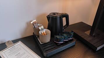 Eine Kaffeemaschine, eine Tasse und ein Tablett mit Teebeuteln auf einem Holztisch.