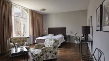 Ein Hotelzimmer mit einem Bett, zwei Sesseln, einem kleinen Tisch, einem Schreibtisch, einer Lampe und einer Zimmerpflanze.