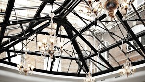 A spacious hall with high ceilings and a glass roof, featuring elegant chandeliers and round tables set for dining.