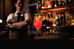 Un bar con un cantinero y un cóctel sobre la barra.