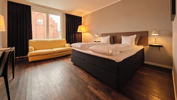 A hotel room with a bed, a sofa, a desk, and a lamp.