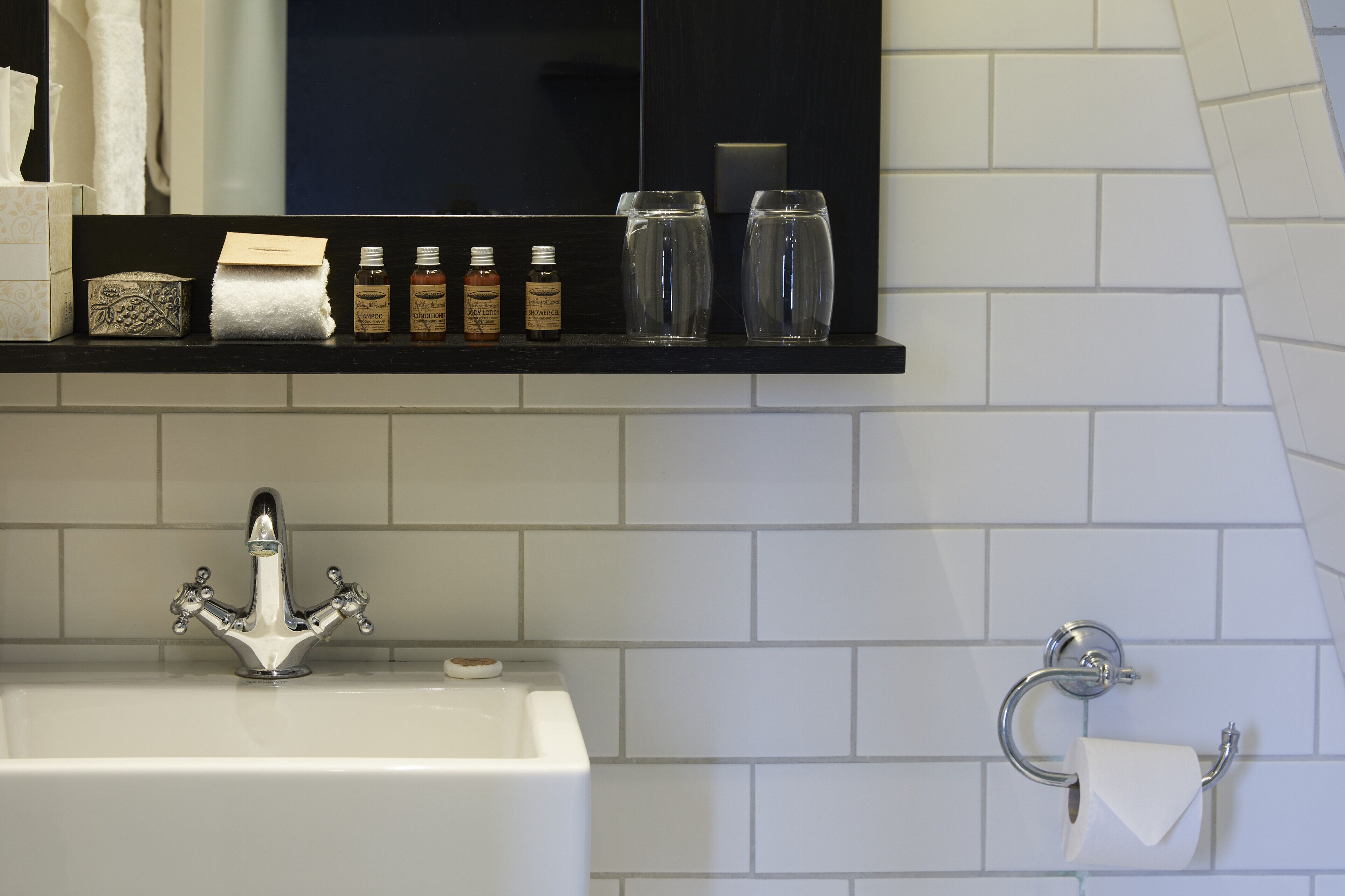Een badkamer met een wit wastafel, een spiegel en een plank met toiletartikelen.