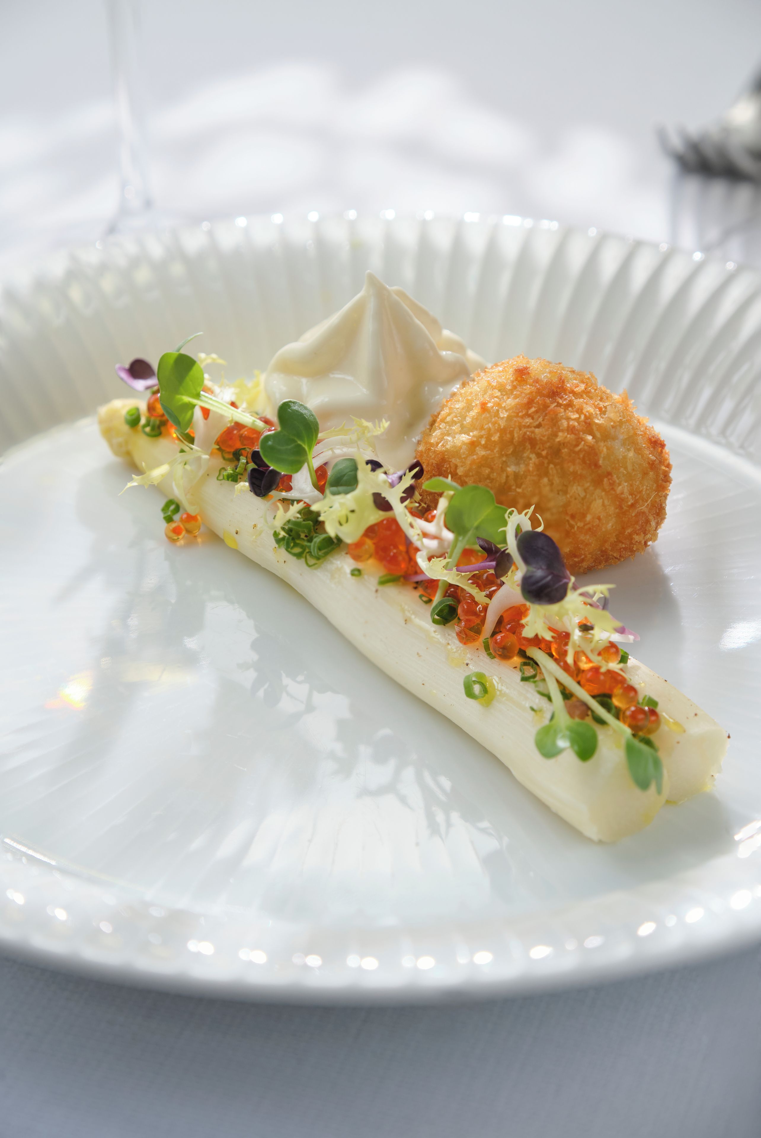 Une assiette blanche contenant un plat composé d’une sauce blanche, de légumes verts et d’un aliment doré et légèrement brun, probablement frit.