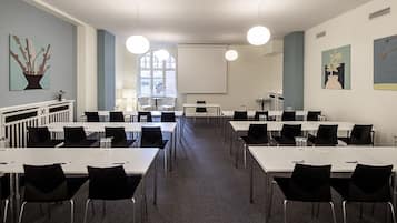 Une salle de conférence avec des tables blanches, des chaises noires et un grand écran.