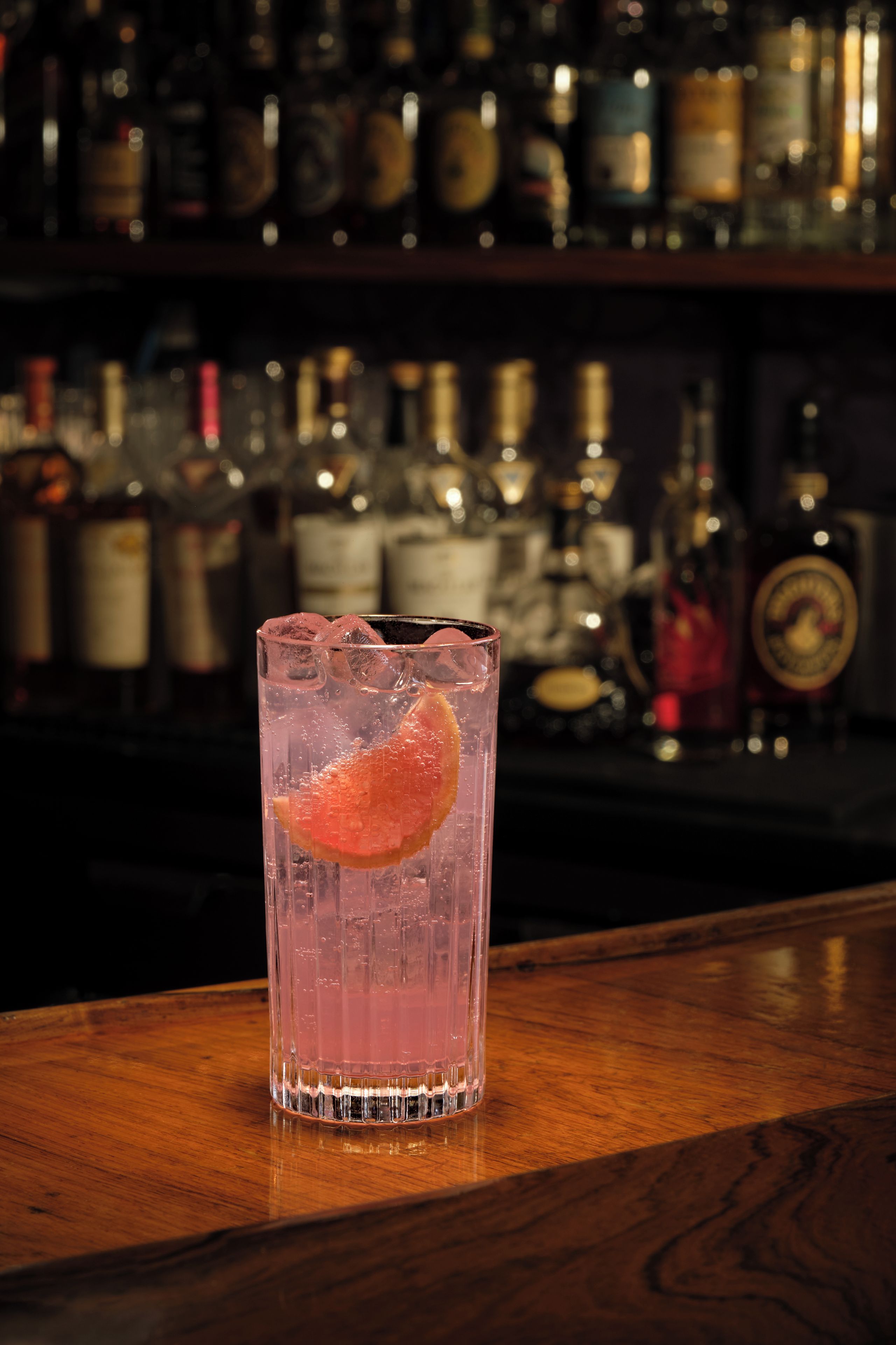 Eine Bar mit einem Glas eines rosa Getränks, Eiswürfeln und einer Orangenscheibe.