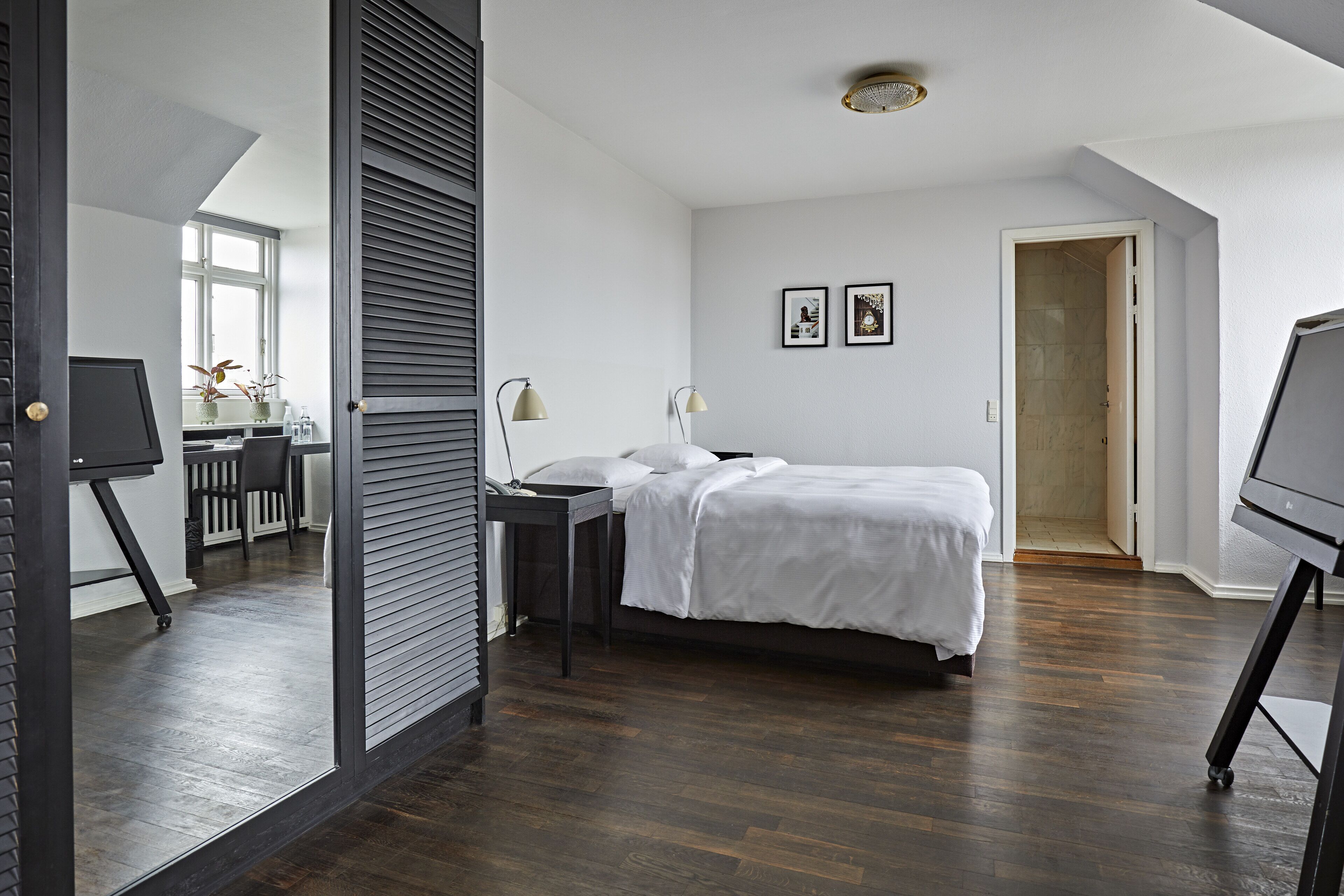 A bedroom with a bed, a desk, a chair, and a large mirror.
