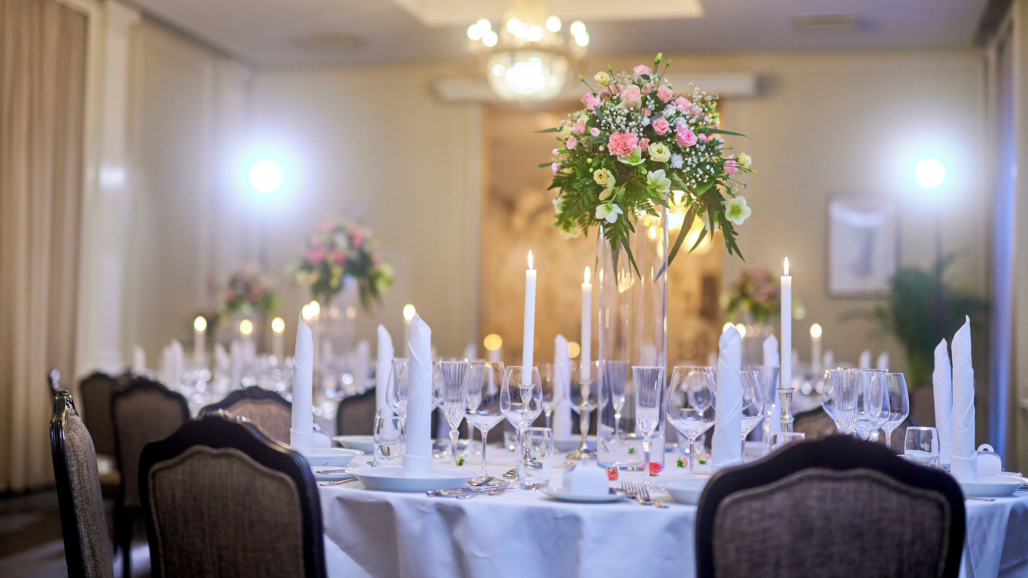 Una sala de banquetes amb taules preparades per a un esdeveniment formal, amb centrals de flors i vetrereria de cristall.