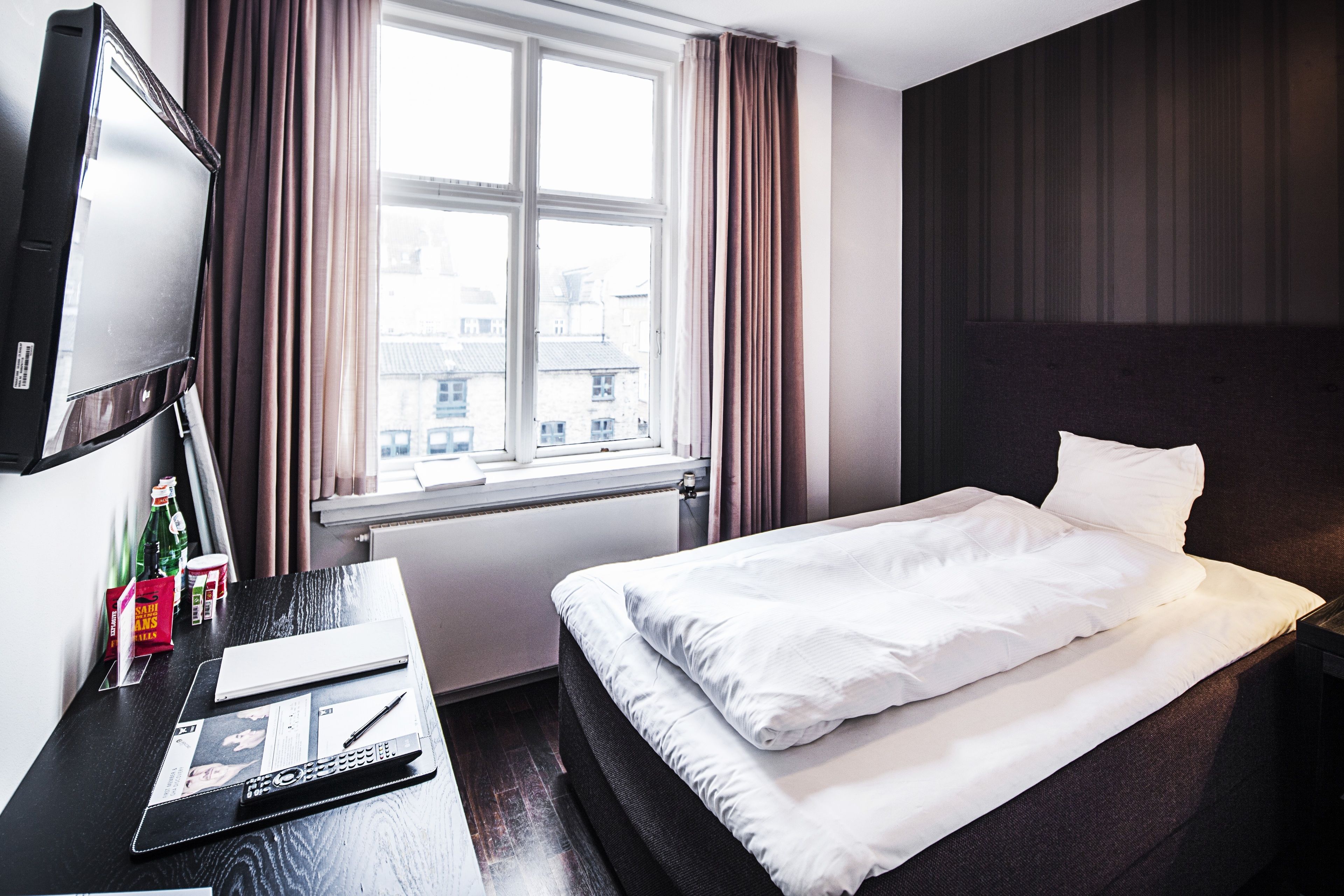Una habitación de hotel con una cama, un escritorio con ordenador, televisión y ventana con cortinas.