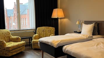 A hotel room with two beds, a chair, a lamp, and a view of a building through a window.