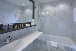Un baño moderno con un lavabo blanco, una bañera y una ducha. Hay artículos de aseo en el lavabo y una toalla colgada en la pared.