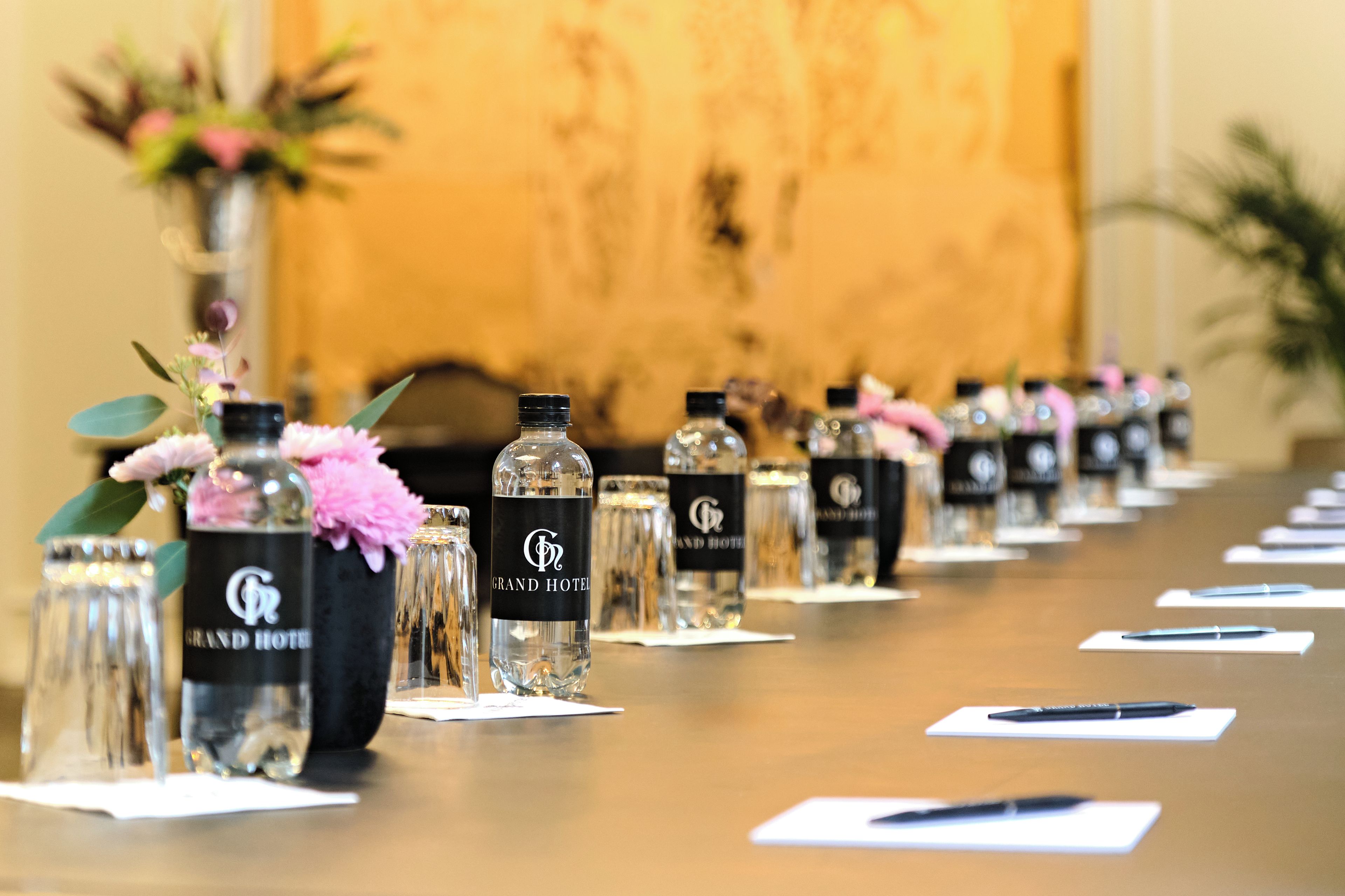 A row of bottles labeled 'Grand Hotel' with a clear glass design, placed on a table with papers and pens.