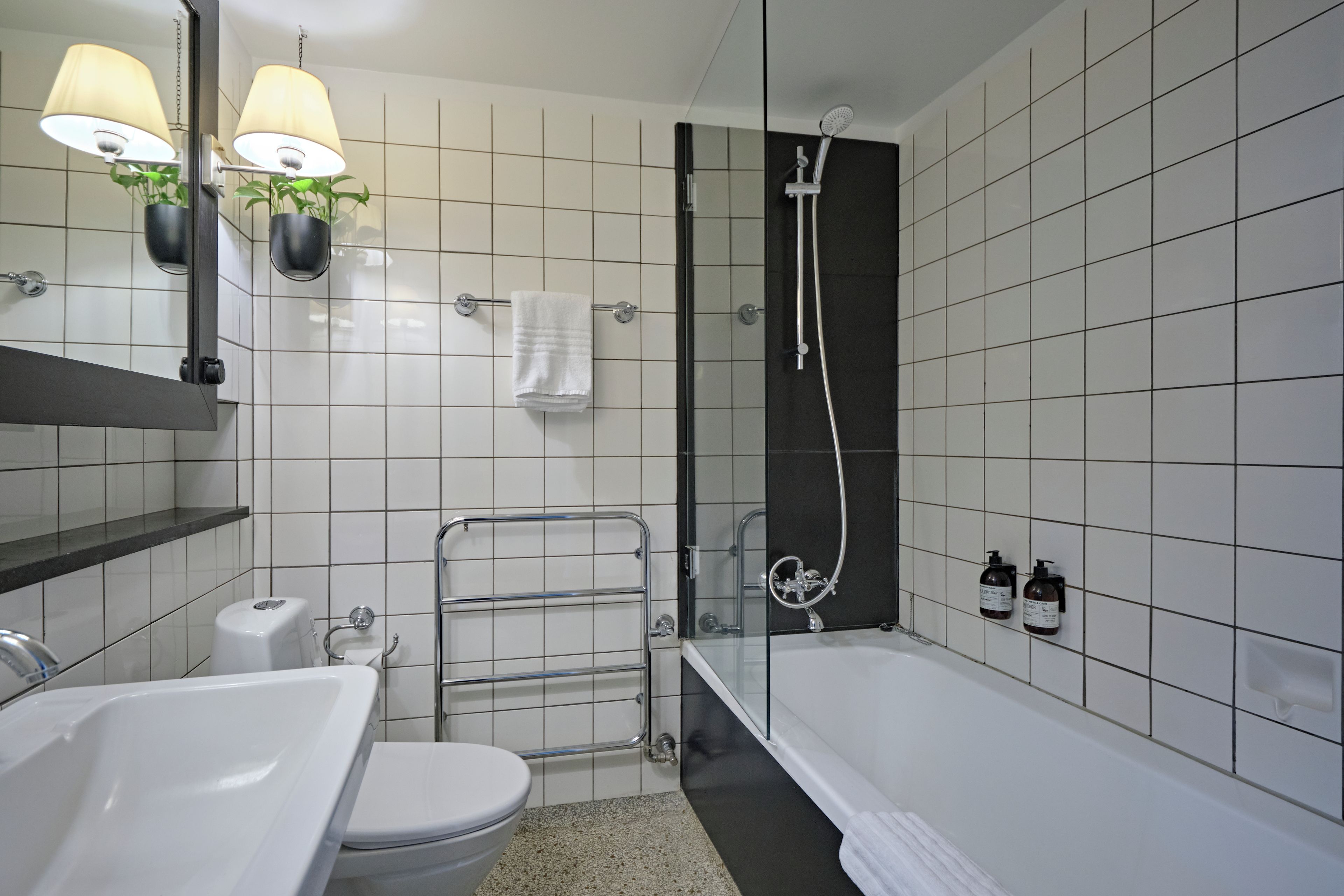 A modern bathroom with a bathtub, toilet, and sink. There are two wall-mounted lamps and a towel rack.
