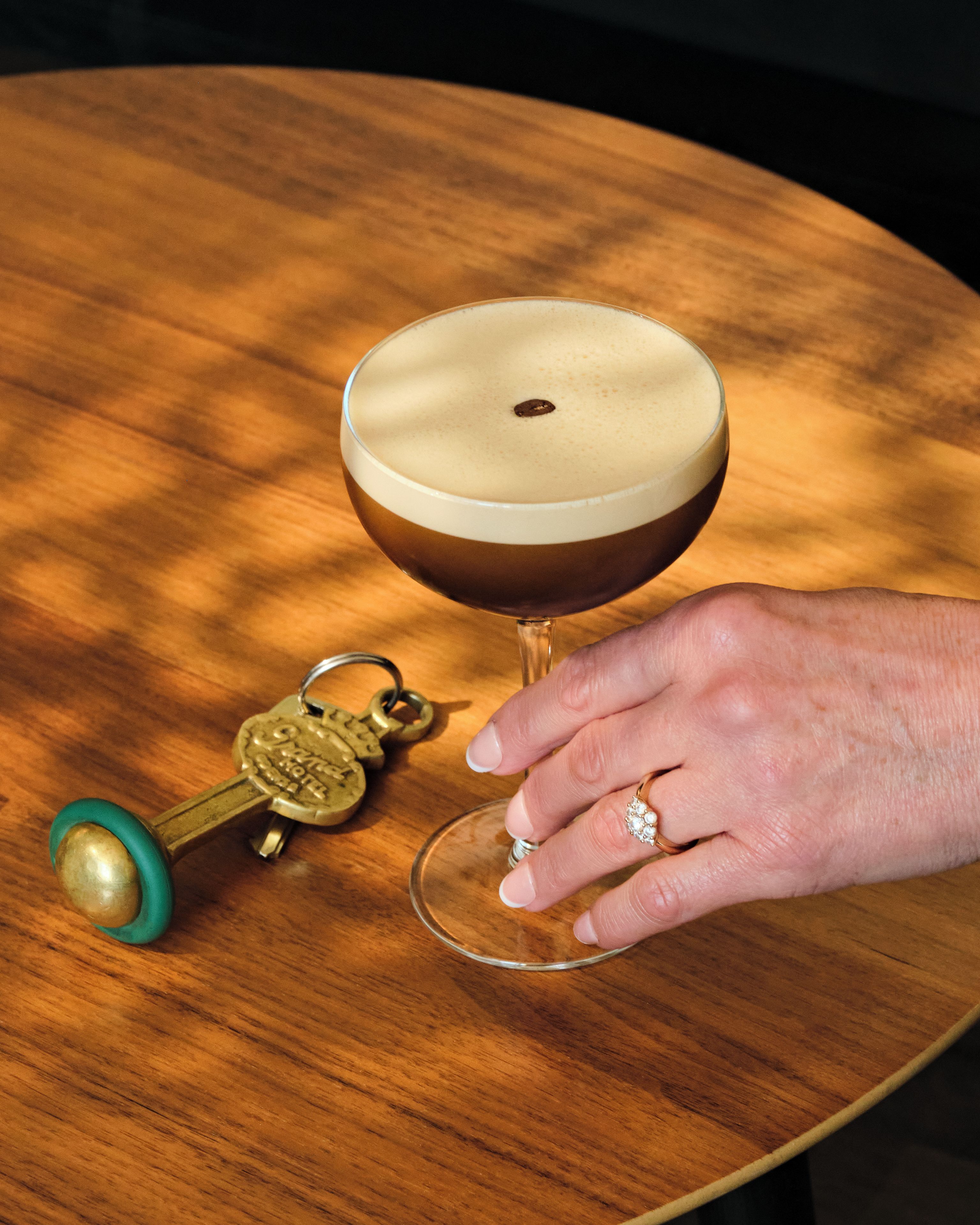 Een hand die een wijnglas vasthoudt op een houten tafel met een sleutelhanger en een flesopener.