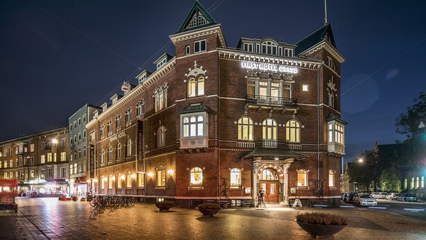 A historic hotel with a prominent tower, large windows, and a well-lit facade.