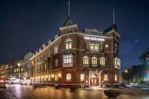 A historic hotel with a prominent tower, large windows, and a well-lit facade.