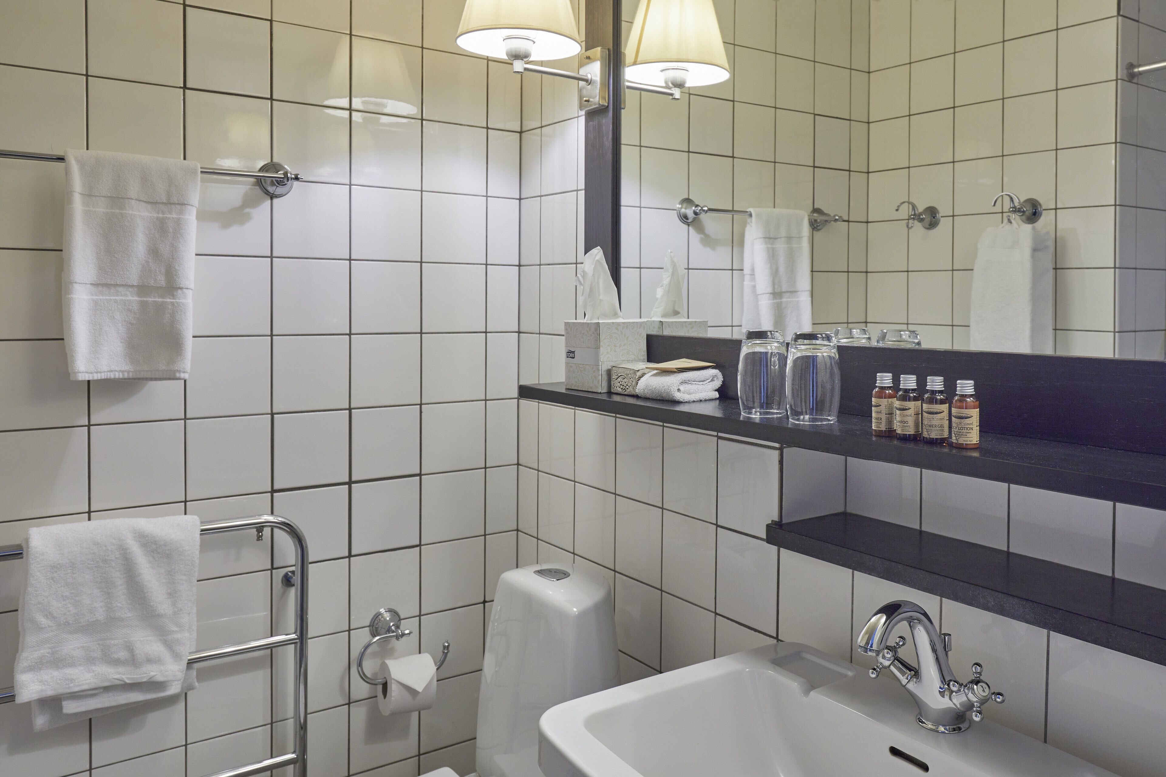 A bathroom with white tiles, a sink, a mirror, and a towel rack.