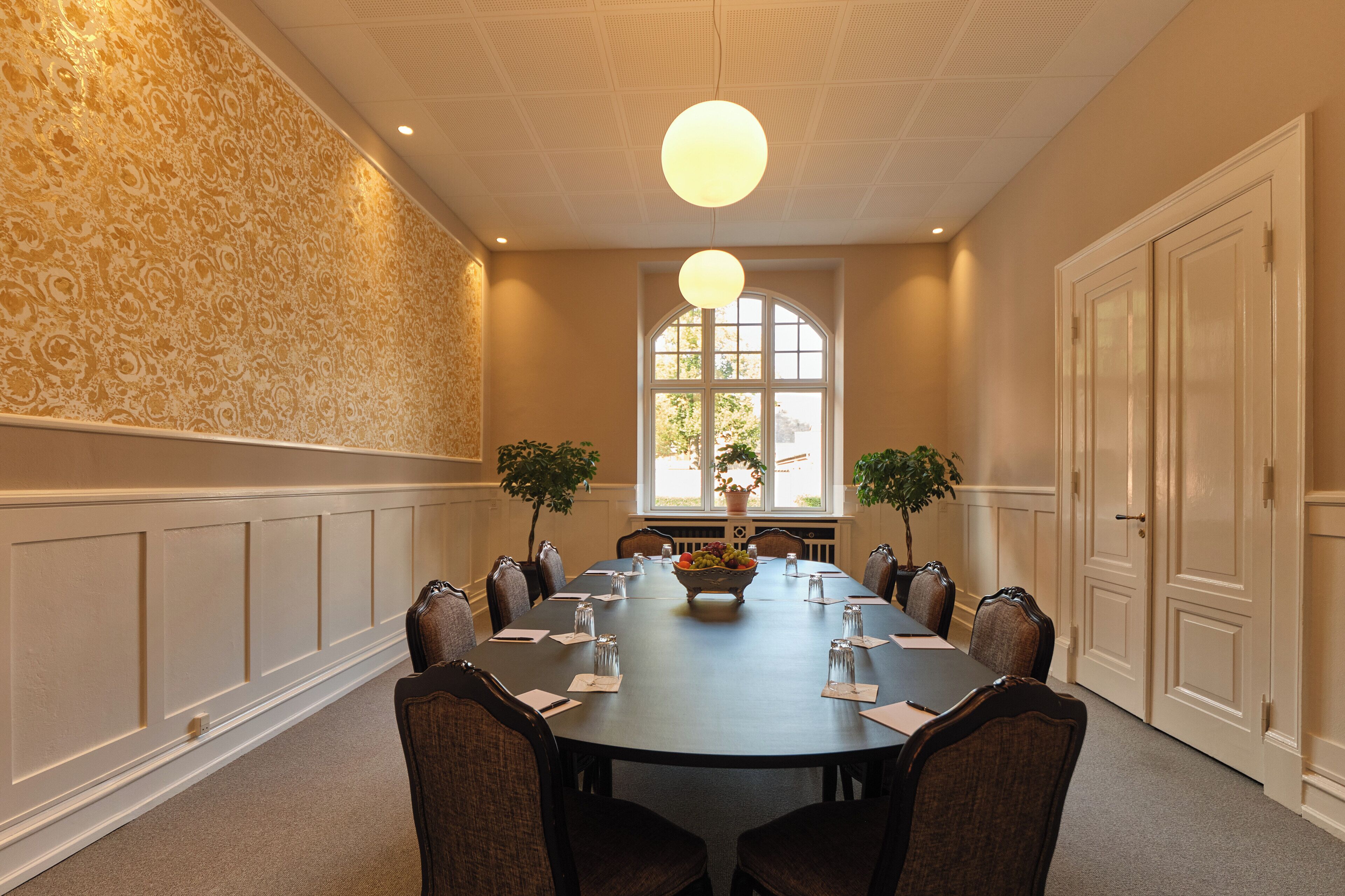 A conference room with a long table, chairs, a chandelier, and two potted plants.