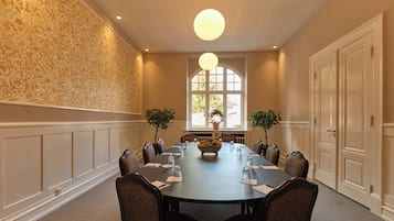 A conference room with a long table, chairs, a chandelier, and two potted plants.