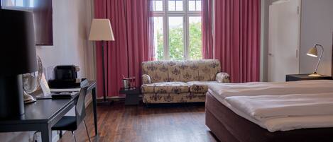 Una habitación de hotel con una cama, un escritorio con computadora, una silla, una lámpara y un ventanal con cortinas.