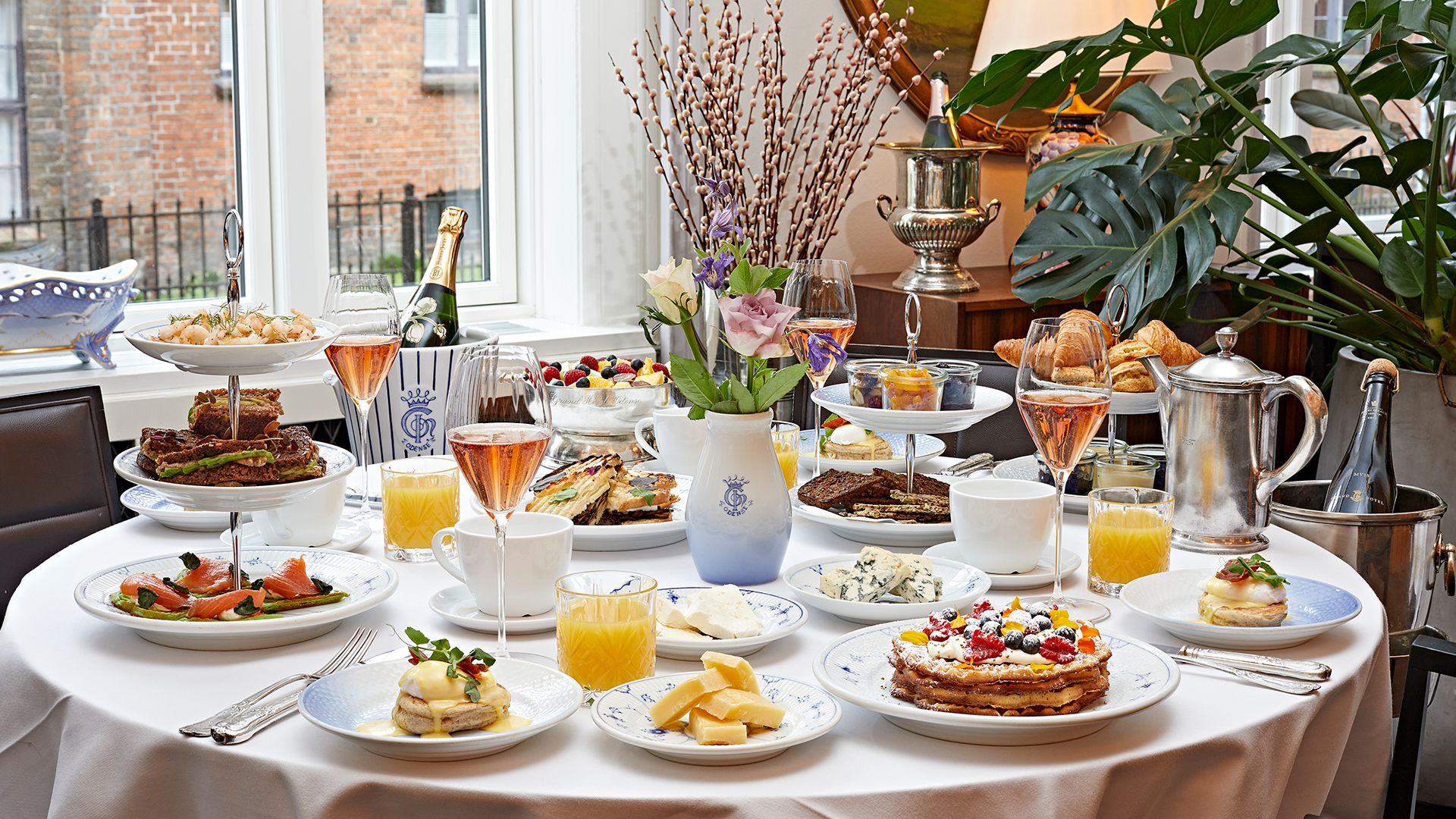 A breakfast buffet with various dishes, drinks, and a vase of flowers.