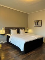 A neatly made bed with white linens, a dark headboard, and two bedside tables with lamps.