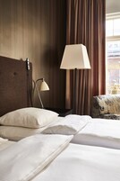Una habitación de hotel con cama, una mesita de noche con lámpara y una ventana con cortinas.
