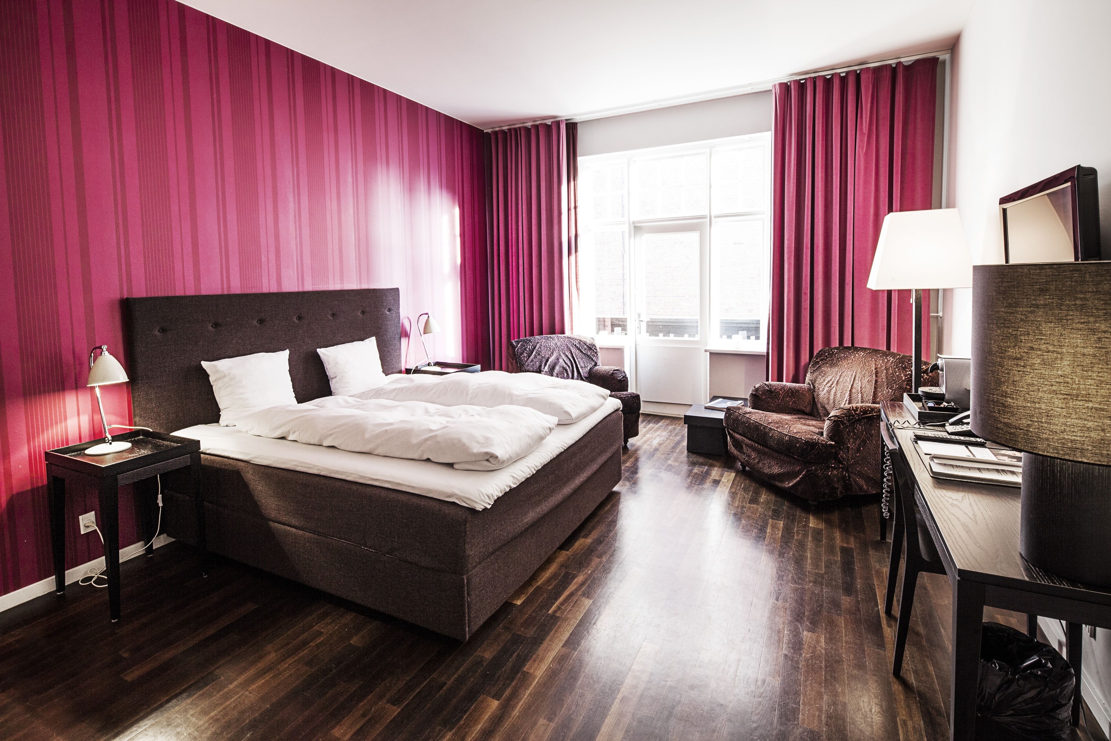 A hotel room with a large bed, a desk, a chair, and a window with curtains.