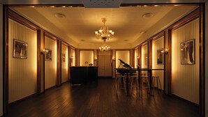A hallway with wooden flooring, a grand piano, and framed pictures on the walls.