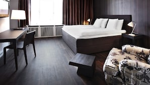 A modern hotel room with a large bed, a desk, a chair, a small table, and a sofa.