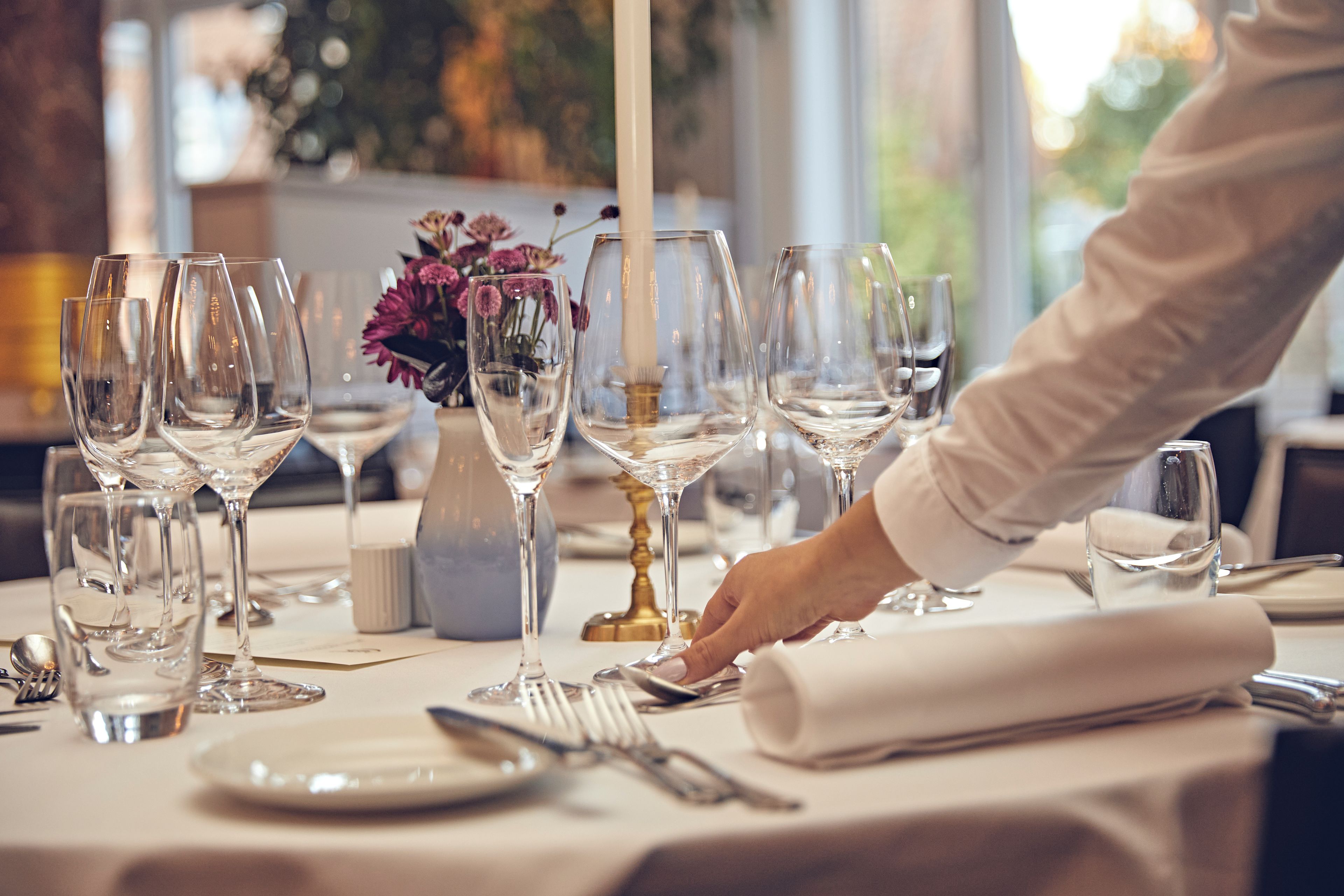 A table set for a meal with multiple wine glasses, a vase with flowers, and a candle.