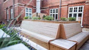 A wooden bench with a slatted backrest and seat, positioned on a wooden deck.