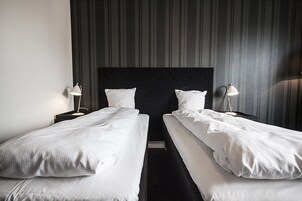 Una habitación de hotel con dos camas individuales, un cabecero oscuro y dos lámparas de noche.