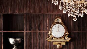 Un reloj de pared con base decorativa, un cuenco de plata en un aparador de madera y una araña con detalles de cristal.