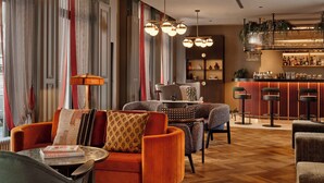 A modern lounge area with a bar, striped curtains, and a mix of seating including a sofa and chairs.