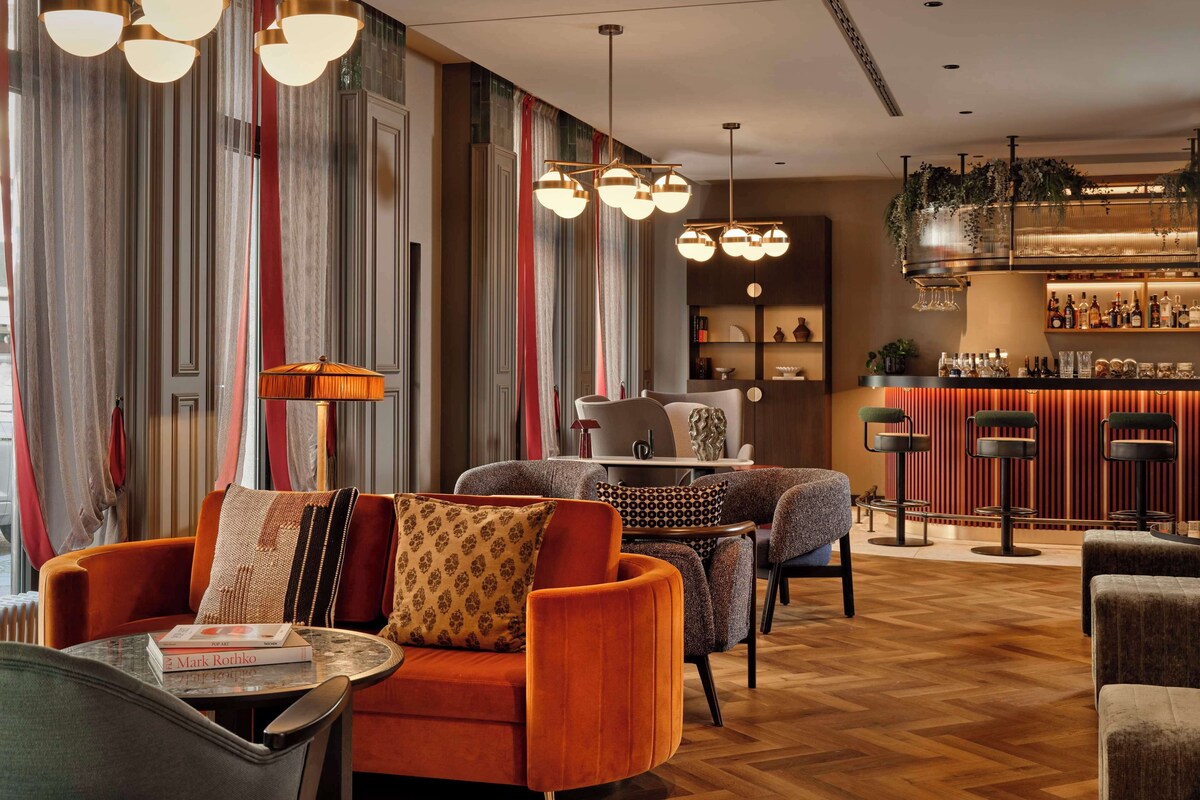 A modern lounge area with a bar, striped curtains, and a mix of seating including a sofa and chairs.