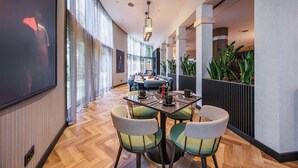 A modern dining area with a long table, four chairs, and a large screen on the wall.