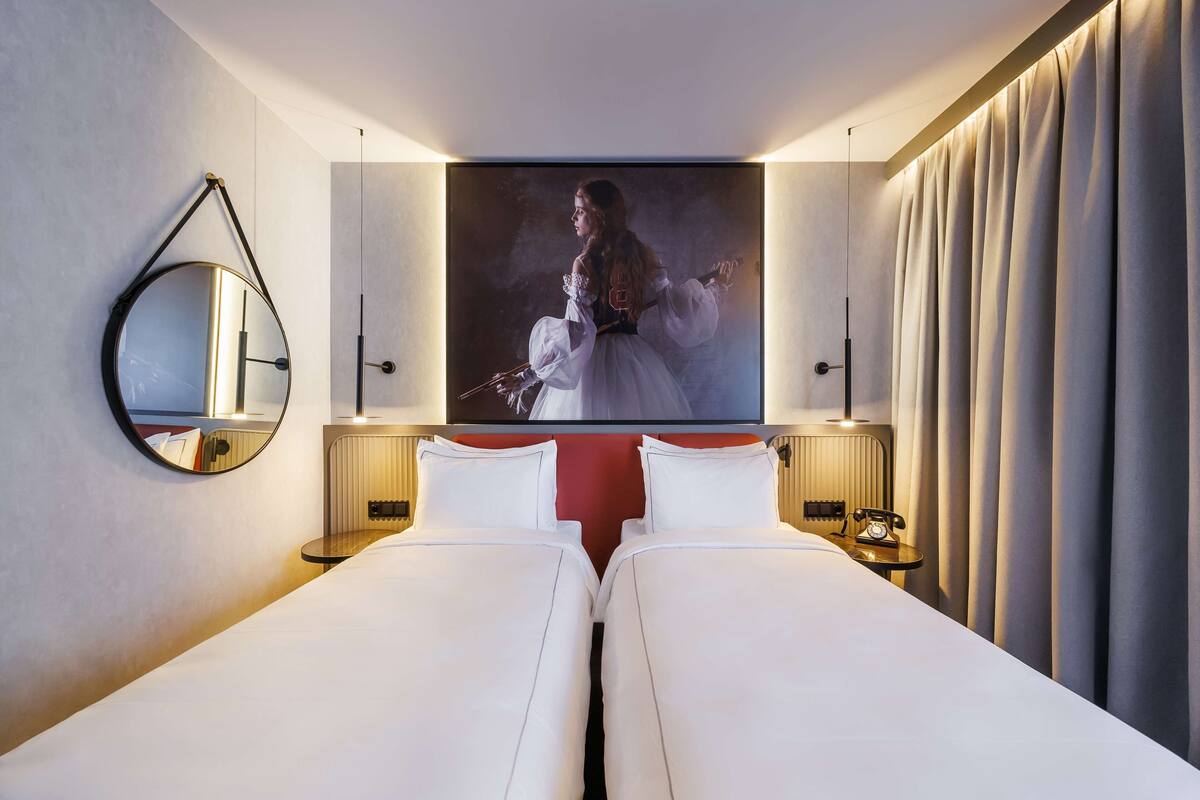 Habitación de hotel con dos camas, un espejo grande, un cuadro en la pared y un teléfono en la mesita de noche.