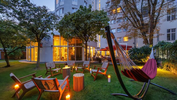 An outdoor seating area with chairs and a hammock, surrounded by trees and a building with glass doors.