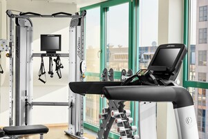 Ein Fitnessraum mit Trainingsgeräten, Laufband und Fernseher.