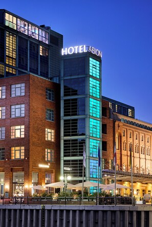 Un hotel con un llamativo letrero que dice 'HOTEL ABION', fachada de vidrio y un edificio de ladrillo adyacente.