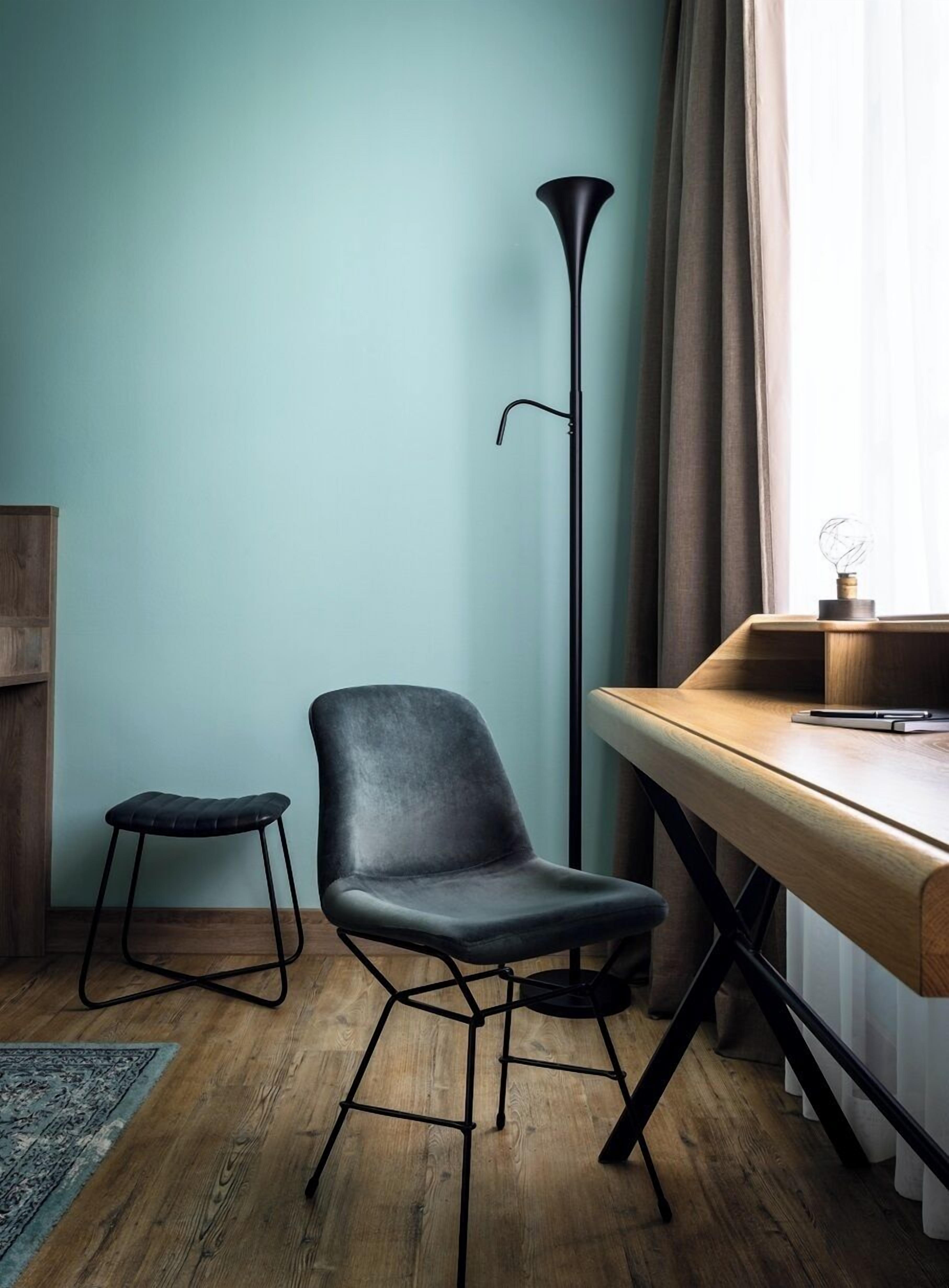 Una habitación moderna con un escritorio de madera, una silla negra, un taburete pequeño y una lámpara de pie alta.